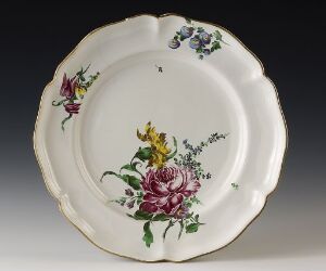  Antique porcelain plate with scalloped edges, featuring a hand-painted floral design with a large pink rose and smaller clusters of blue, purple, and yellow flowers with green leaves.