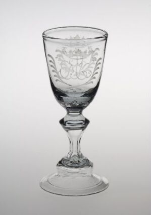  Clear glass goblet with ornate etching on the bowl and a decorative stem, positioned against a plain, light background.