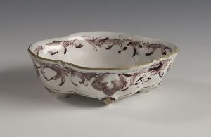  An oval-shaped, shallow ceramic basin with irregular edges, showing off-white coloring adorned with abstract purple floral patterns and a slightly glossy finish. Artist name and title are unknown.