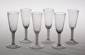  Five clear champagne glasses with beaded stems, aligned in a row on a reflective surface with a soft grey gradient background.