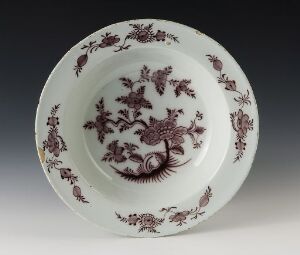  An antique white ceramic plate with detailed iron-red floral patterns in the center and around the rim on a neutral gray background. Artist name and title are unknown.