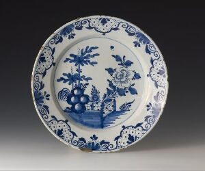  A delicately designed blue-and-white porcelain plate featuring a central floral or pastoral motif, surrounded by an ornate border with intertwined flowers and foliage, set against a neutral background. Artistname and title are unknown.