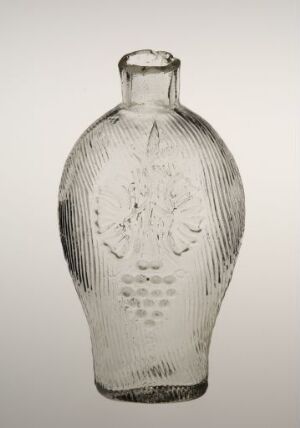  A transparent glass bottle with detailed embossed patterns, featuring a central emblem with symmetrical designs, displayed against a light grey background.