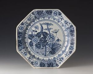  An octagonal blue and white porcelain plate with a central floral design and intricate border patterns set against a gray background. The artist name and title are unknown.