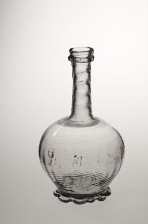  A clear, hand-blown glass bottle with a round base and narrow neck, displaying subtle imperfections and air bubbles, set against a gradient of light grey to white background.