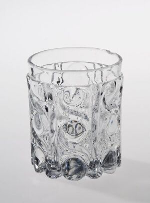  A clear glass tumbler with an intricate embossed design, standing upright against a plain, light background.