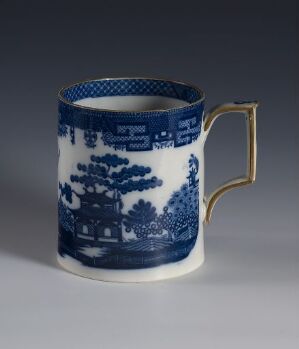  A porcelain mug titled "Willow" with a classic blue-and-white design depicting landscapes and willow trees, featuring a contrasting golden handle, against a gradient gray background. Artist name unknown.