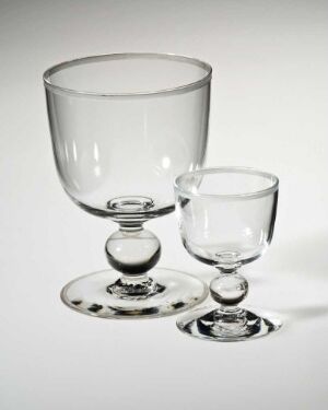  A set of two clear, etched glass vessels by Hadeland Glassverk, including a smaller goblet and a larger glass, against a white background. They display refined craftsmanship and are made for dining and serving purposes. The objects reflect and refract light, appearing luminous and elegant.