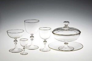  A collection of seven clear glassware items, including a cylindrical cup, one larger and three small stemmed glasses, and a covered dish, arranged on a light grey background.