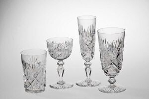  A set of four intricate cut crystal glasses on a light background, including a short tumbler, a champagne flute, a wine glass, and a tall highball glass, each with detailed patterns.