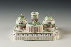  An antique porcelain inkstand with a pastel palette featuring muted pinks, greens, and gold accents. The symmetrical design includes a central inkwell with two smaller compartments, all adorned with intricate floral patterns and resting on a rectangular base with decorative edges.