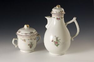  A white porcelain teapot and sugar bowl set with delicate floral designs and patterned bands in reddish-brown and gray, accented with gilding. Both items have lids topped with small knobs. They are displayed against a neutral gray background.