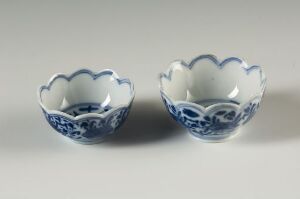  Two small blue and white porcelain bowls with scalloped edges and intricate patterns, set against a light grey background.