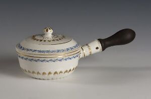  A vintage white enameled saucepan with delicate blue patterns and a wooden handle, set against a light grey background.