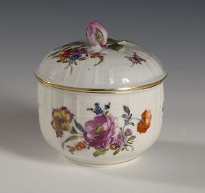  A small, round porcelain container with a matching lid, intricately painted with detailed and colorful floral designs, and gold trim around the edges; the lid is topped with a painted pink floral bud-shaped handle. Artist name and title remain unknown.