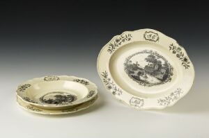  Two pieces of antique-style cream-colored ceramic tableware with black pastoral scenes and decorative borders on a neutral light-gray to white gradient background.