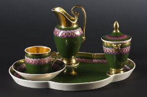  An exquisite porcelain tea set comprising a green teapot, sugar bowl with a lid, and a cup, all adorned with gold details and pink floral patterns, arranged on an oval serving tray against a dark background.