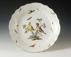  An ornate scalloped ceramic plate featuring an intricate depiction of two birds surrounded by foliage and insects, with a color palette of soft yellows, browns, greens, and hints of blue and red against a white background.