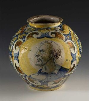  An intricately designed, bulbous vase with a narrow opening, displaying a realistic portrait of a bearded man in profile within a circular medallion, surrounded by blue and white floral patterns on a yellow background.