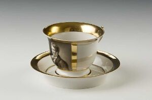  A feldspar porcelain cup and saucer with gold accents and gray hand-painted overglaze decoration, titled "Bertel Thorvaldsen" by the Den kgl. Porcelainsfabrik, presenting a luxurious and ornate design. The cup features a reflective gold rim and handle, with gray decorative panels between the golden bands.