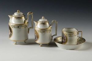  A set of three porcelain tea service pieces on a light grey background, including two tea pots and a tea cup with saucer, all white with gold trim and violet and green floral patterns.