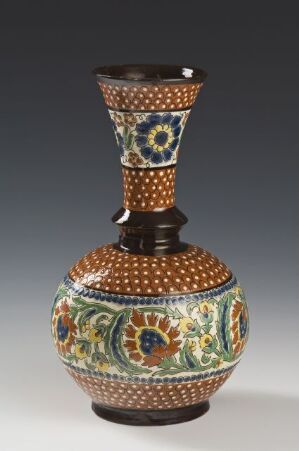  An intricately patterned vase with a bulbous body and flared neck, showcasing detailed floral medallions in blue, green, orange, and white against a dark background.