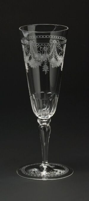  A clear, etched champagne flute with a delicate, intricate design on the upper bowl, slender stem, and round base, standing against a dark background.