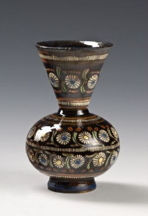  An ornate vase with a flaring neck and bulbous body, featuring dark earthy tones and detailed floral patterns in greens, reds, and cream colors.