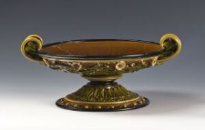  An antique bowl with decorative golden details and handles on a solid base, featuring dark green and gold colors against a gray background.