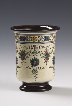  A cylindrical ceramic vase with a flared base and rim, featuring a symmetrical pattern of blue flowers, golden yellow accents, and green leaves on a creamy background, set against a graduated gray backdrop.