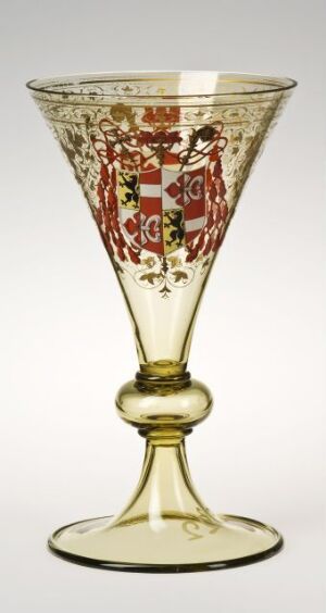  An intricately designed glass goblet with a conical bowl intricately decorated with red, white, and green heraldic patterns and a yellow-tinted stem and foot, set against a light background.