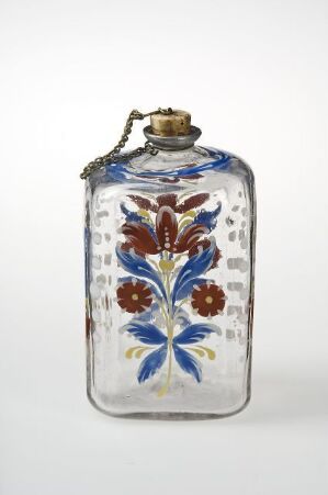  An antique glass bottle with rounded corners and a textured surface, featuring a hand-painted floral pattern in blue, white, and orange, topped with a brass-colored metal cap with a chain.