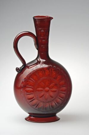  A dark red glass vessel with a round body and sunburst pattern, featuring a narrow neck and a single handle, set against a neutral background.