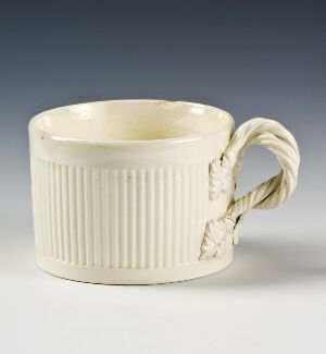  An off-white ceramic mug with vertical ribbing on the body and a handle designed to look like a twisted or braided rope on a light gray background.