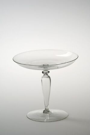  A clear glass coupe with a wide, shallow bowl, slender stem, and circular base stands against a white background.