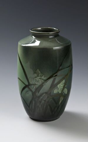  A tall, slender green vase with a glossy finish, featuring subtle, shadowy images of leaves and branches on its surface, evoking a serene, natural scene. Artist name and title are unknown.