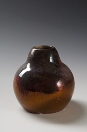  An asymmetrical ceramic vase with a glossy brown to amber gradient glaze, displayed against a softly lit gray gradient background.