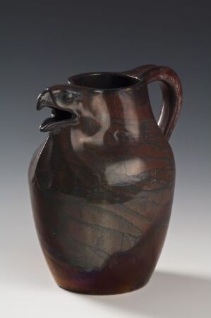  A glossy mahogany brown ceramic jug with a curved handle and a tapered silhouette against a muted grey background.