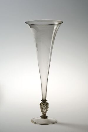  A tall, clear glass, trumpet-like vessel with a flared opening, a decorative band around its narrow stem, and a disc-shaped base, set against a gradient white-to-gray background. Artist name and title unknown.