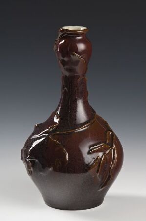  A glossy, deep brown ceramic vase with a spherical body and slender neck, featuring organic leaf-like impressions on its surface against a gray background. Artist name and title are unknown.