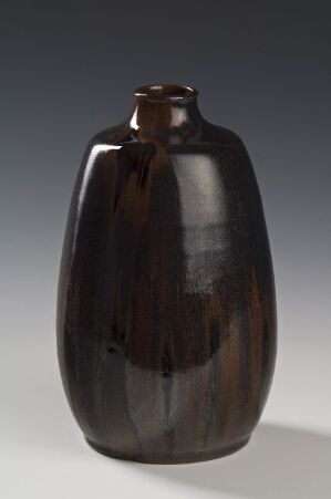  A tall, slender, glossy ceramic vase with a narrow opening at the top, colored in a gradient from dark to lighter brown, set against a soft grey background.