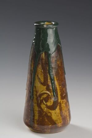  A ceramic vase with a fluid blend of emerald green melting into earthy browns and pops of mustard yellow, evoking a sense of dynamic movement. The vase tapers from a broad base to a narrow top and has a glossy finish. Artist name and title are unknown.