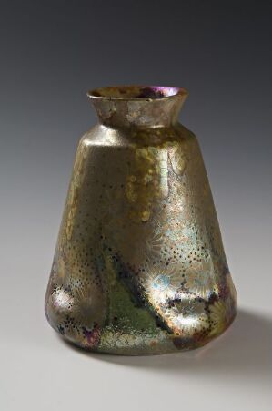  An iridescent, metallic-hued vase with a mottled pattern of olive green and gold, accented with speckles of pink and teal, gently curves into a flared opening, set against a neutral background. Artist name and title are unknown.