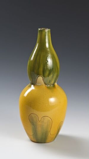  A tall, two-toned ceramic vase, with a bulbous golden-yellow base that transitions into a slender olive-green neck, featuring a subtle green tulip-like design near its base, all against a neutral gray background.