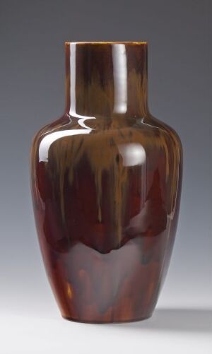  A tall, slender vase with a glossy brown glaze, ranging from caramel to deep espresso tones, reflecting light elegantly on its surface against a neutral background. Artist name and title are unknown.