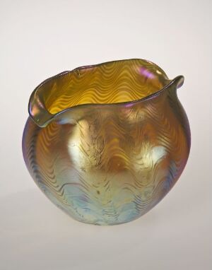  An iridescent hand-blown glass bowl by Lötz, featuring an organic shape with a wavy pattern and a spectrum of colors from amber and yellow to hints of purple, blue, and green that change with the light.