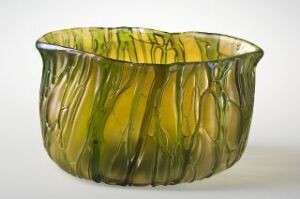  A semi-translucent glass vessel with a freeform, asymmetrical shape featuring shades of olive green, chartreuse, and golden yellow. The vessel has vertical ridges reminiscent of natural organic features, presented against a light gray background.