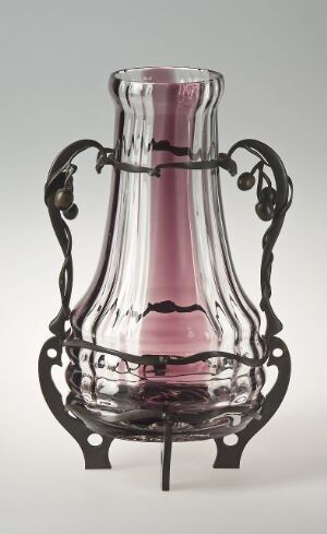  An elegant fluted glass vase with a pink gradient, encased in a dark intricate metal framework with scroll-like designs, set against a neutral background. Artist name and title are unknown.