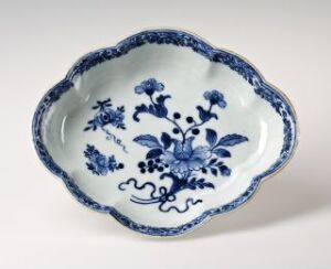  A scalloped-edge ceramic plate featuring a detailed blue floral pattern on a white background, indicative of a traditional style possibly similar to Delftware or Chinese porcelain.