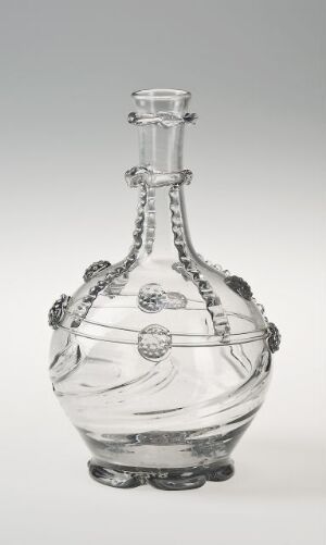  An ornate, clear glass decanter with circular medallions and delicate swirl patterns etched onto its bulbous body and narrow neck, against a bright, uniform background.